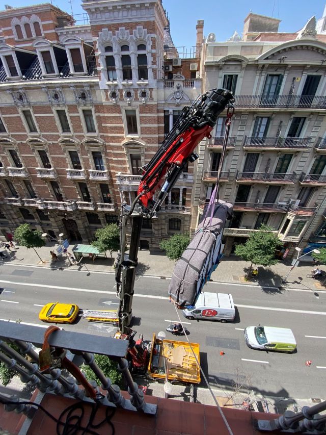 Grúa elevando un piano envuelto por la fachada de un edificio en Barcelona