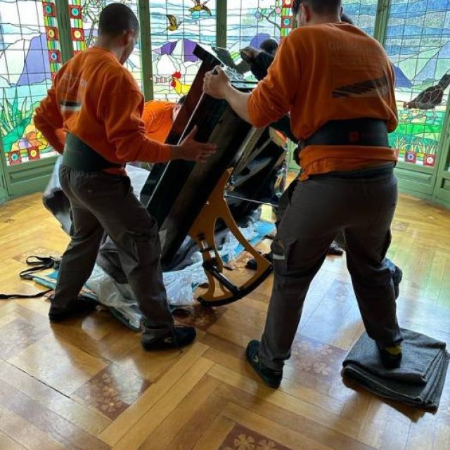 Equipo profesional girando un piano con herramientas especiales para conservar su perfeto estado en el movimiento